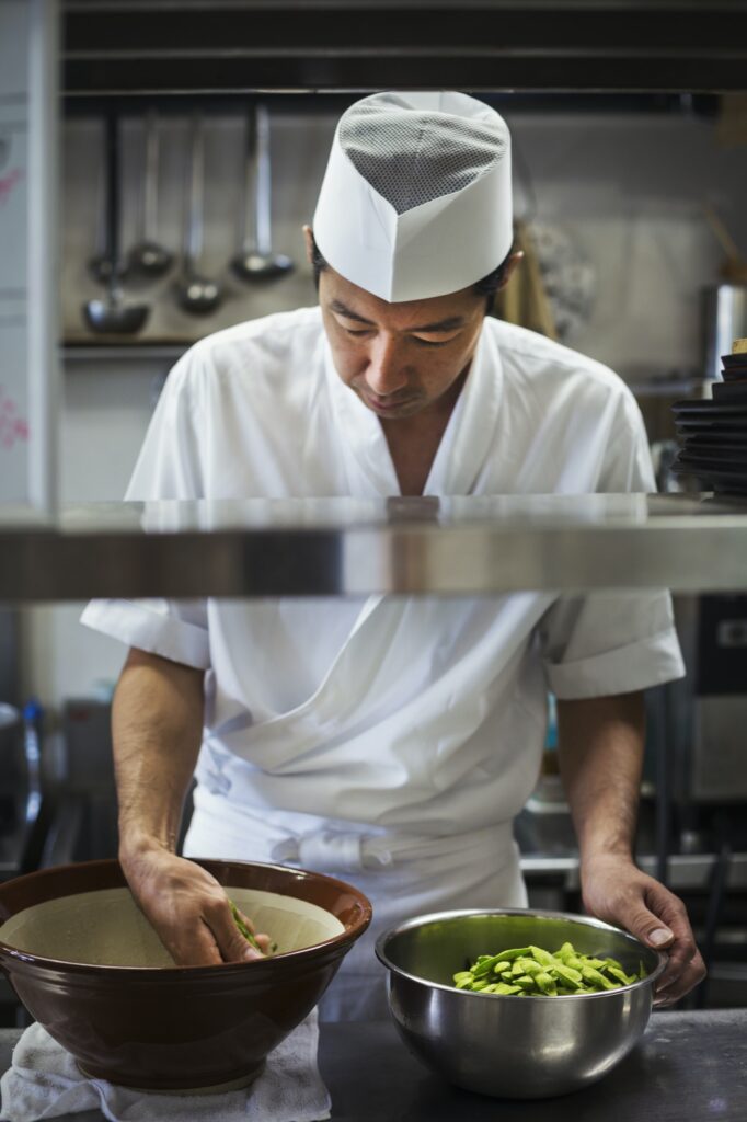 Chef working in the kitchen of a Japanese sushi restaurant, preparing bowl of edamame beans.