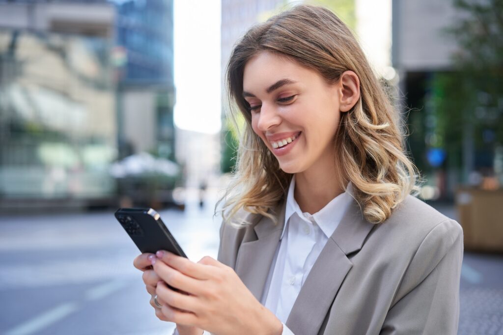 Portrait of smiling businesswoman chat in app, looking at smartphone with pleased face, order